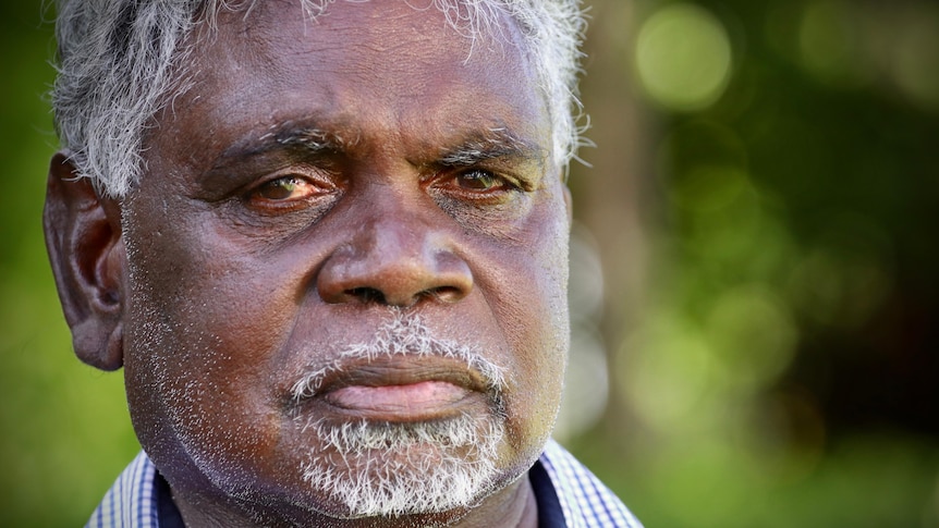 An elderly Indigenous man wearing a suit looks at the camera
