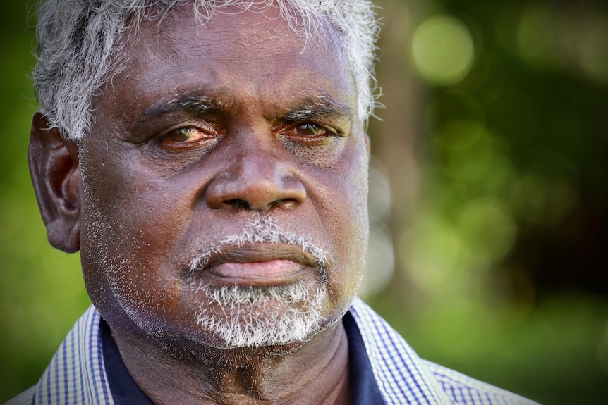 An elderly Indigenous man wearing a suit looks at the camera