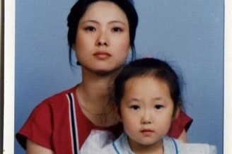 A young Asian woman holds a little girl on her lap in a formal pose