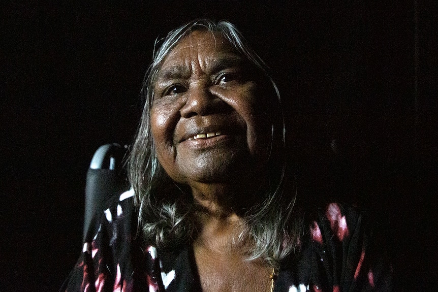 An elderly woman wearing a black patterned top and smiling.