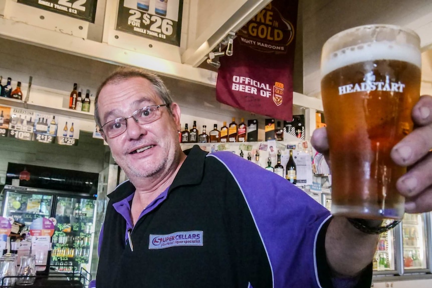 A man stands in a pub holding a beer towards the camera.