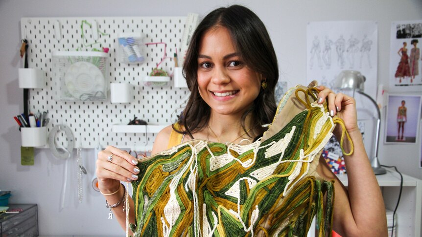 A young woman holds an item of clothing she created. 