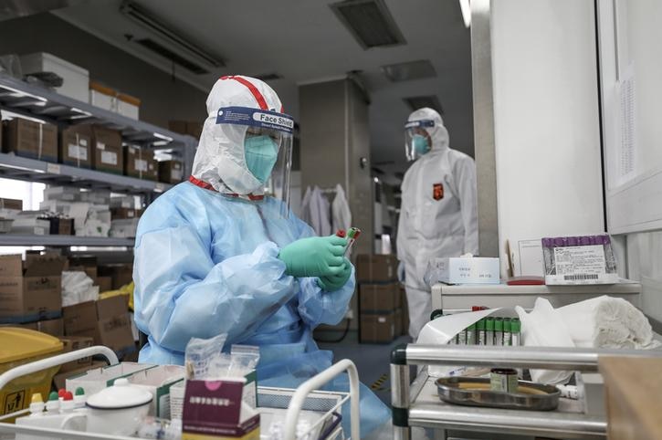 Two scientists in protective gear examining a vial