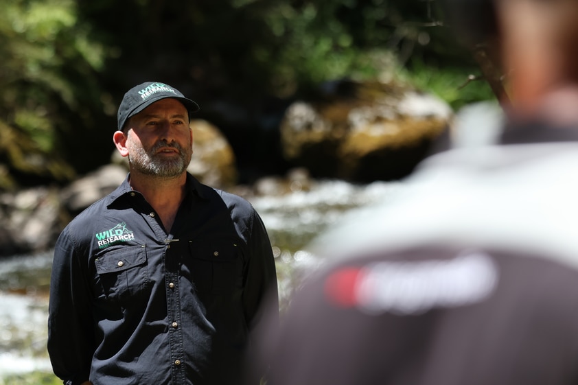 A man in a navy shirt and cap standing in front of a stream. 