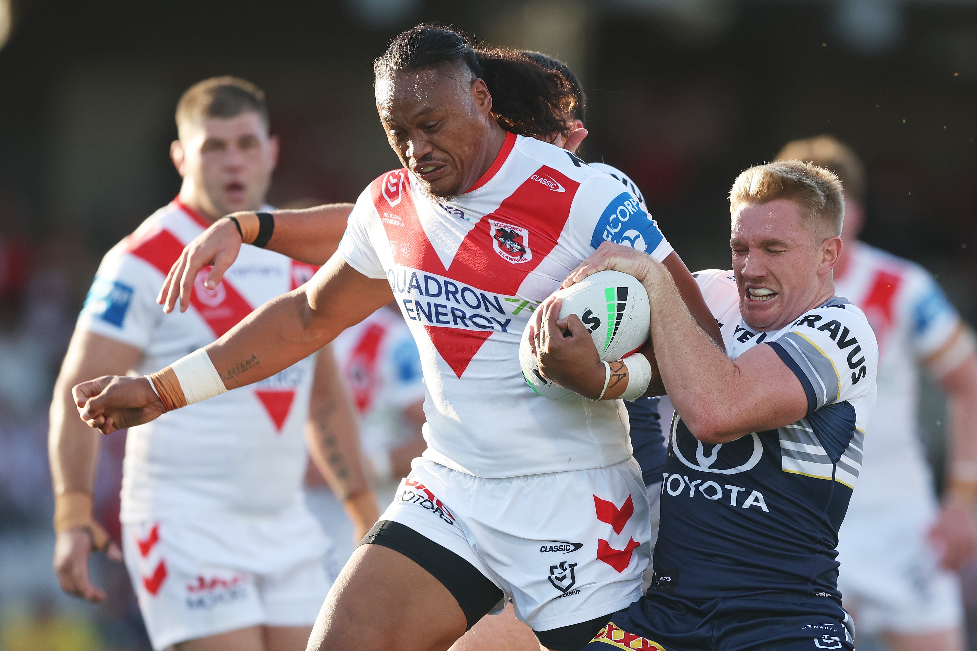 A rugby league player in white and red charges through a tackle