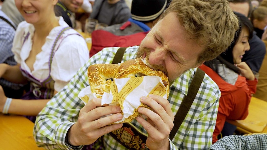 A man enthusiastically holds a giant pretzel in both hands and bites into it at Oktoberfest, Munich.