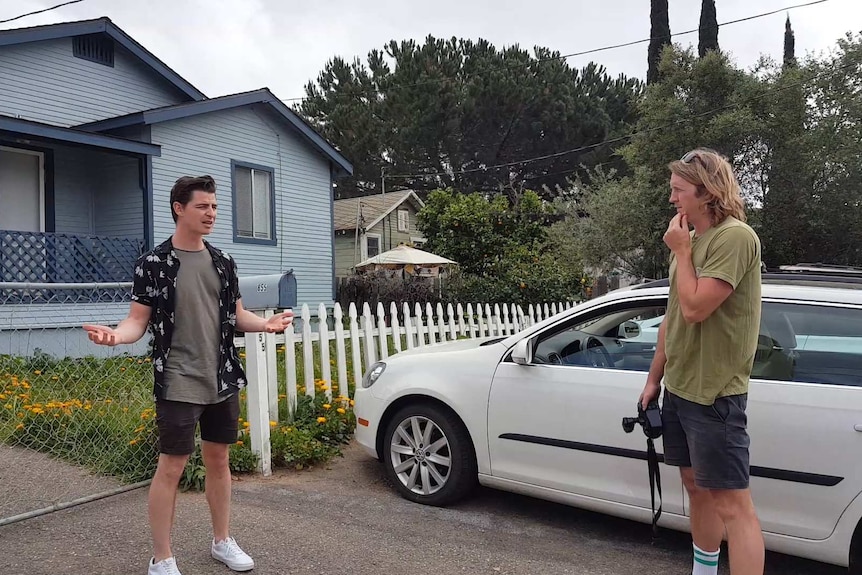 Two men arguing out the front of a blue house.