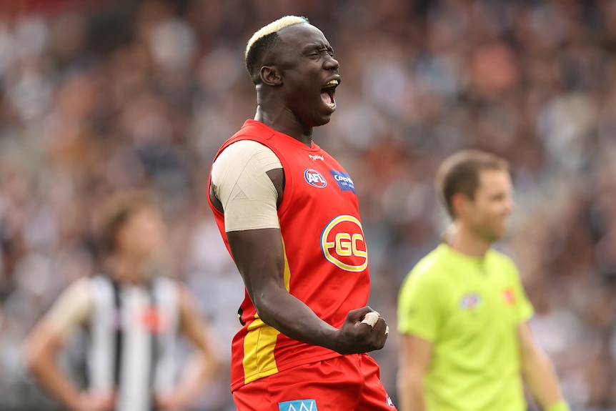 A man wearing a Gold Coast Suns shirt celebrates on field.