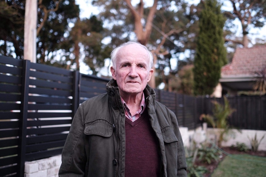 An elderly man looks at the camera in his garden