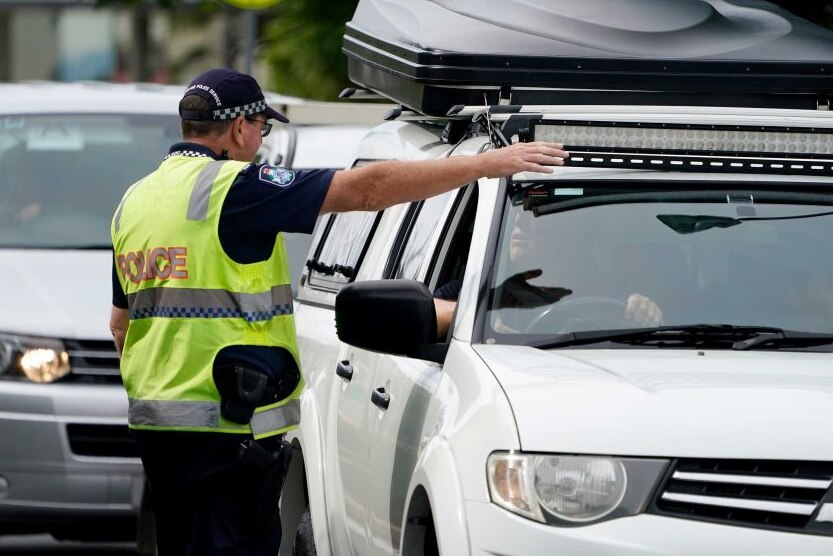 A police officer raises his arm beside a stopped car.