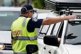 Queensland police officer directs motorists at a border checkpoint on the Queensland-NSW border.
