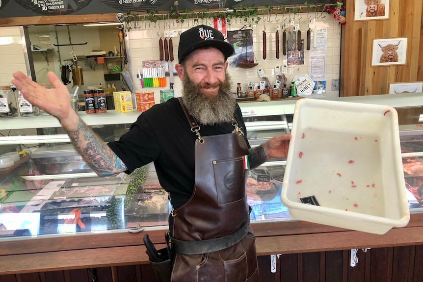 A man with a beard holds up an empty tray of mince.