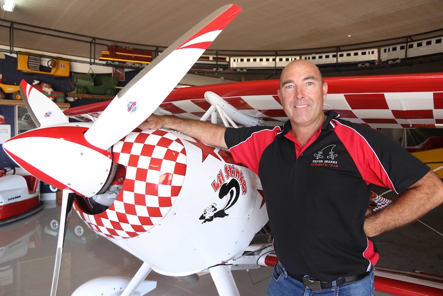 Man on tight shown waist up hand on small white with red check feature aeroplane fuselage near propeller