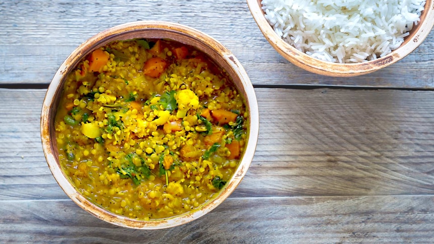 Overhead photo of a vegetable dahl alongside a bowl of white rice, a delicious winter recipe.