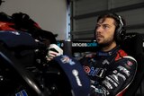 A serious-looking Supercars driver sits in his simulator in full gear during an online race.