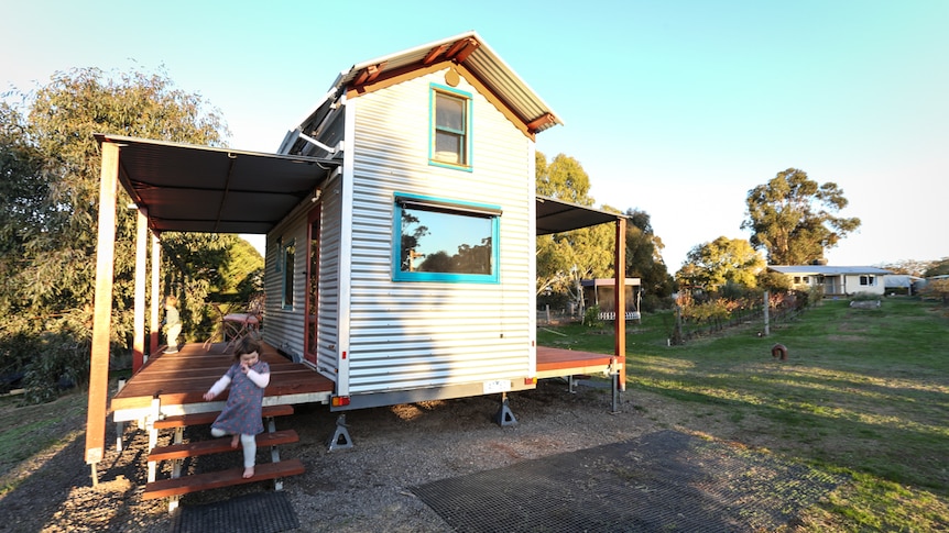 A small weatherboard house with a little girl near the verandah.