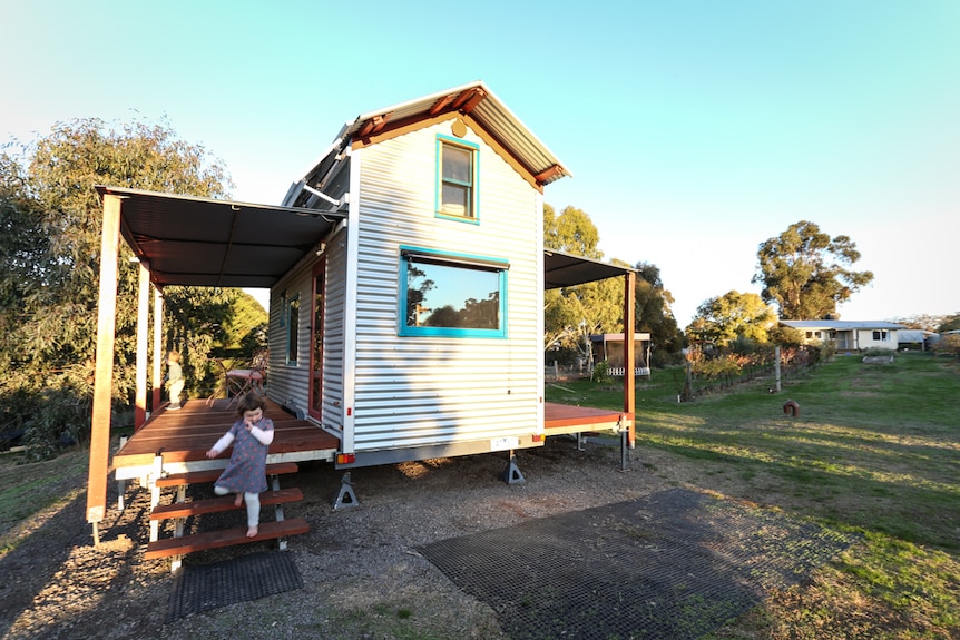 A small weatherboard house with a little girl near the verandah.