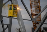 a crane with two men working saw into the bridge