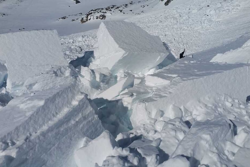 A man surrounded by massive blocks of snow with a large pole.