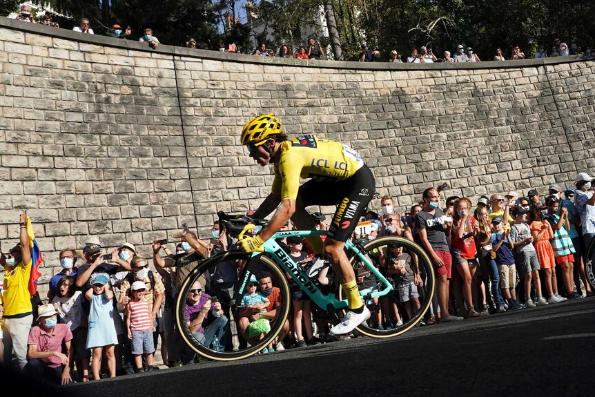 A cyclist wearing yellow rides around a corner with a big crowd watching at the Tour de France.