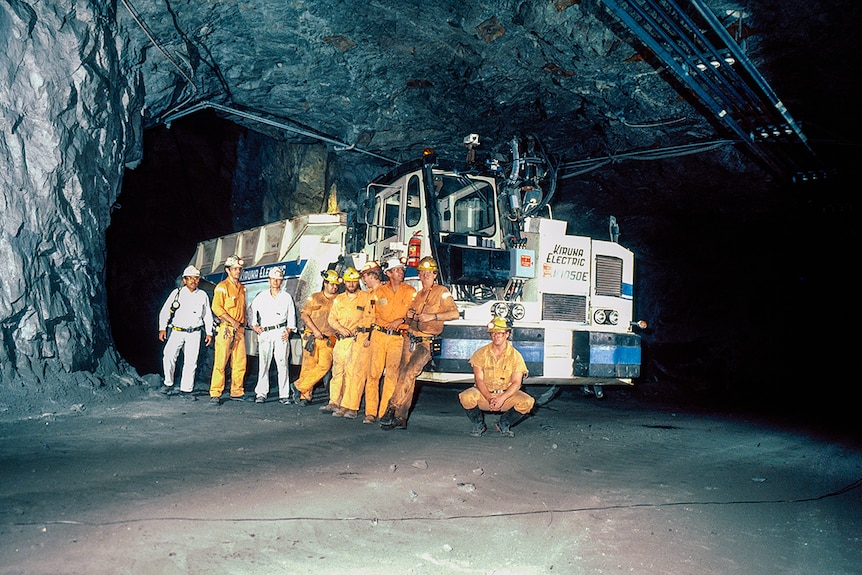 Группа шахтеров под землей с большим грузовиком.