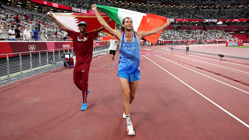 Two smiling athletes walk together on the Olympic track in Tokyo, one carrying the Qatar flag, the other the Italian. 