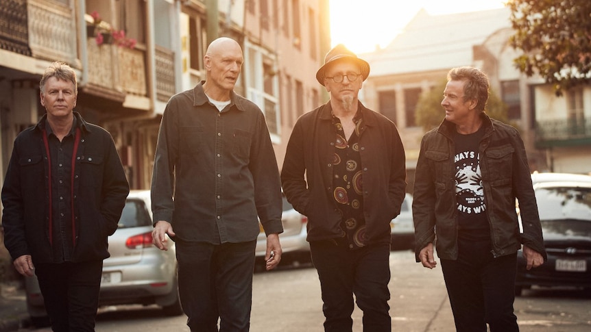 Four members of Midnight Oil walk down a street as the sun sets behind them