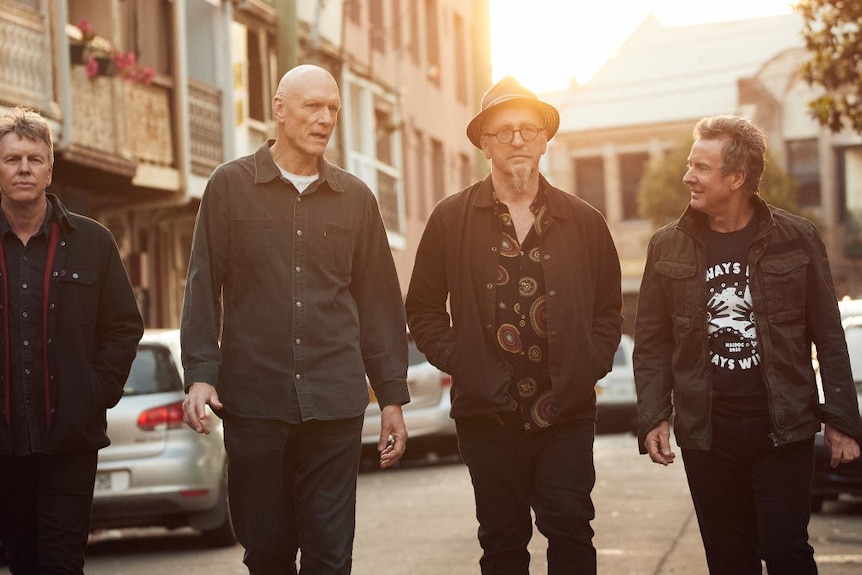 Four members of Midnight Oil walk down a street as the sun sets behind them