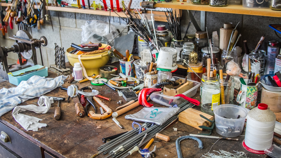 The workbench is cluttered with handles, frames and accessories for each of the umbrellas created within the workshop.