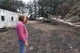 Photo of a farmer: Marilyn Mullan as she looks at the fire destruction around her farm