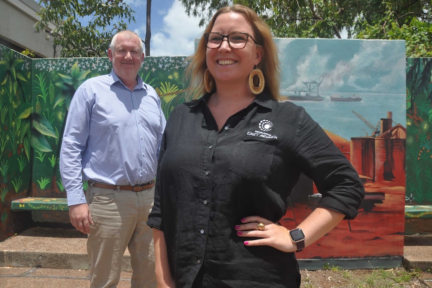 Jordy Bowman has one hand on her hip and smiles at the camera. Behind her, Jim Rogers is wearing a button down shirt and smiling