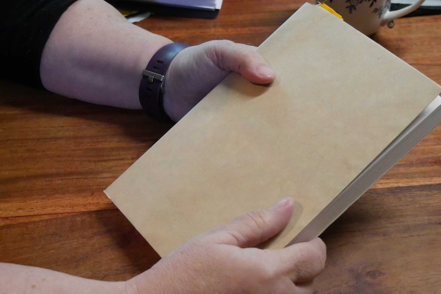 A woman's hands holds a book that has been covered in brown paper.