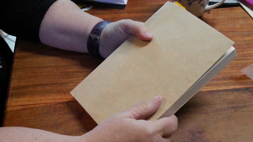 A woman's hands holds a book that has been covered in brown paper.