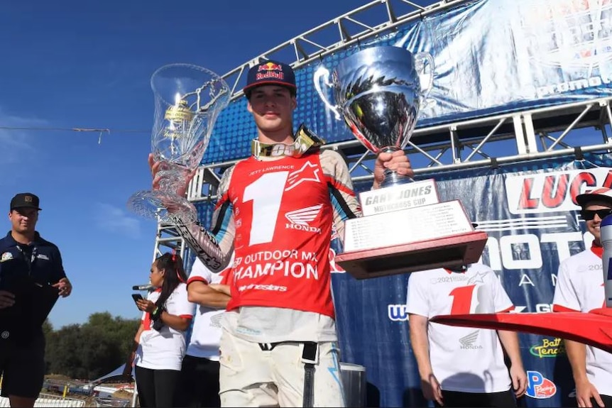 Young motocross race stands on podium holding two trophies