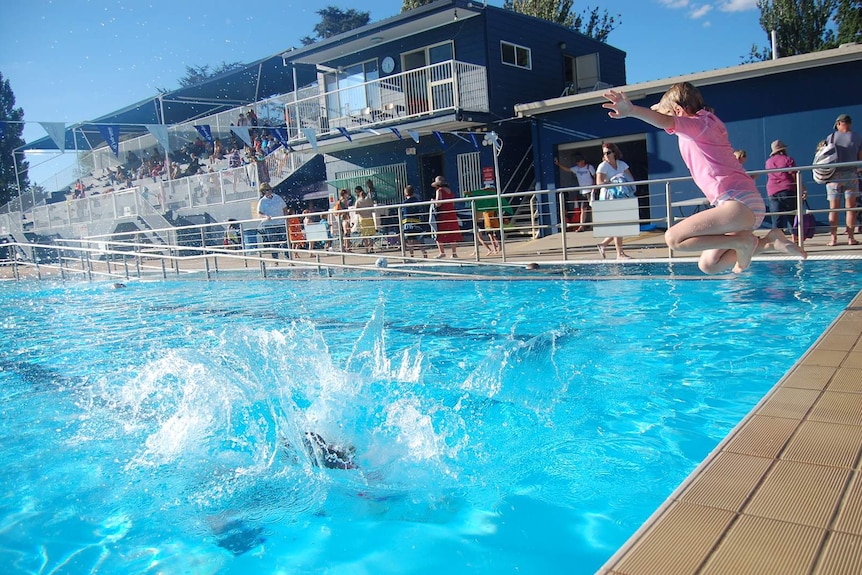 A child jumping into a public pool with a splash from a child that has already jumped in