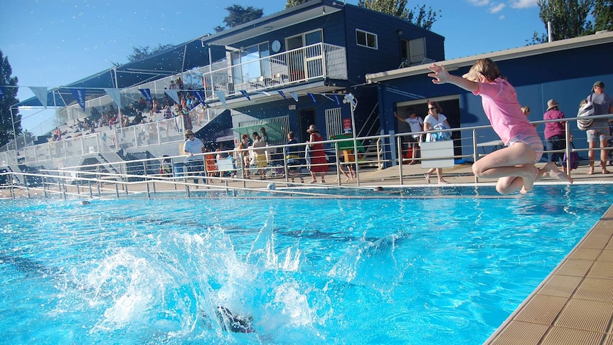 A child jumping into a public pool with a splash from a child that has already jumped in