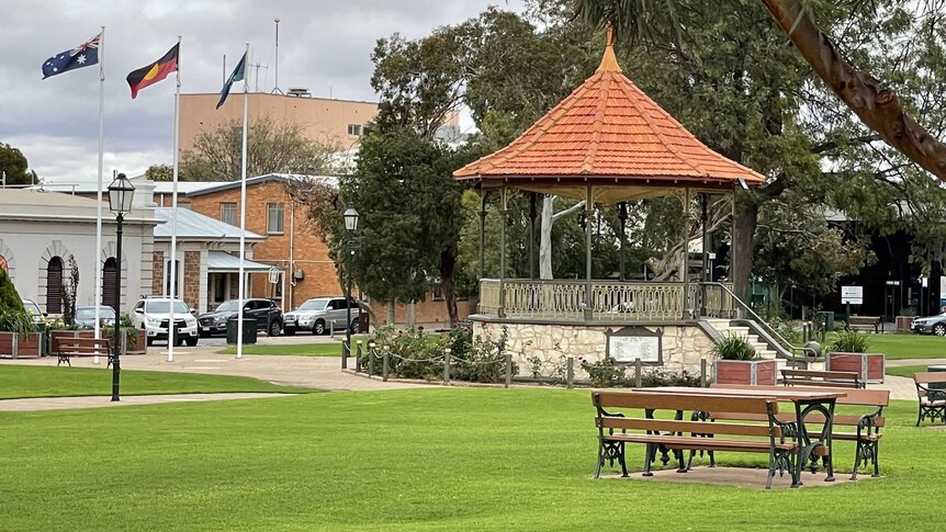 A public space featuring a lawn, park benches and a rotunda. Australian and Aboriginal flags fly nearby.