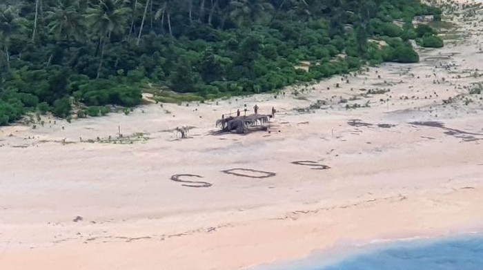 A wide beach. A helicopter is to the left and an SOS message in large writing to the right