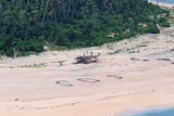 A wide beach. A helicopter is to the left and an SOS message in large writing to the right