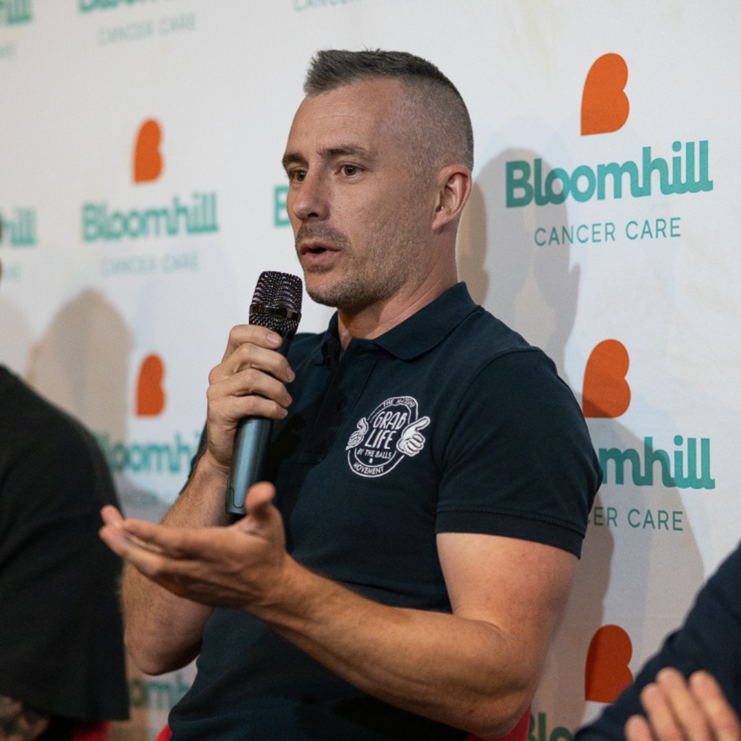 Un hombre vestido con una camisa negra se para frente a una multitud con un micrófono. 