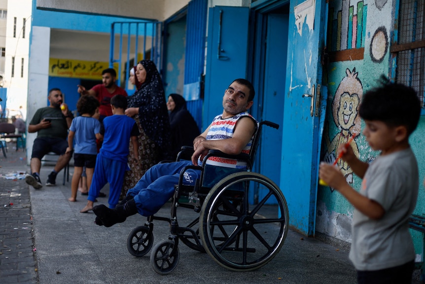 A person sitting on a wheelchair and children in a shelter. 