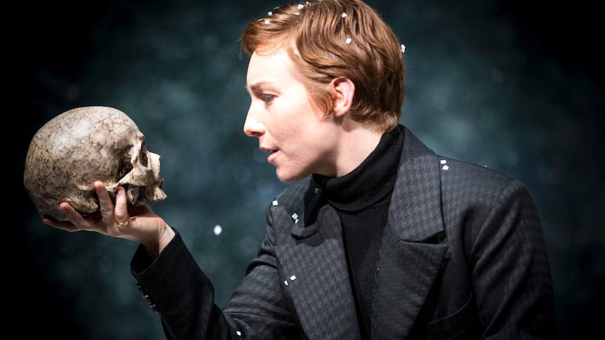 Harriet Gordon-Anderson in a grey suit looks at a human skull she is holding in her hand.