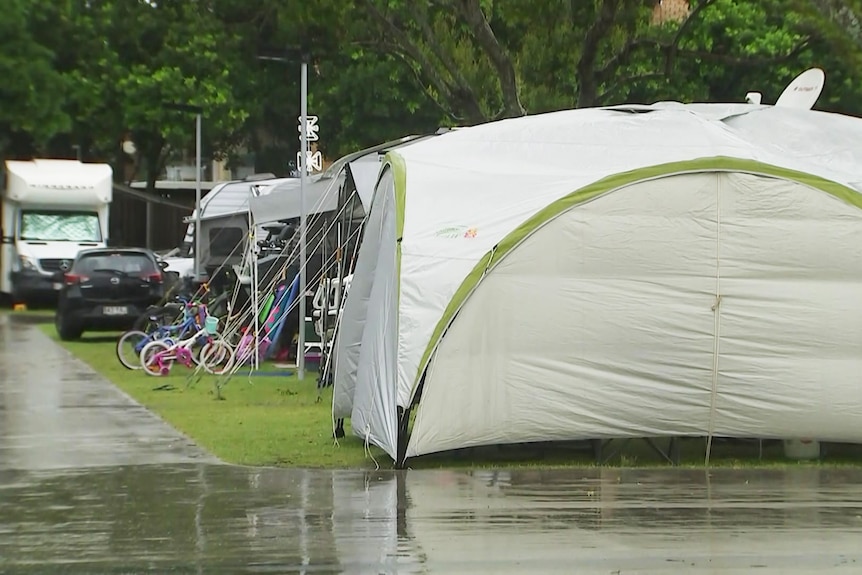 A row of tents and campervans with rain falling on the concrete pathways.
