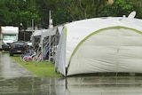 A row of tents and campervans with rain falling on the concrete pathways.