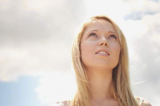 Young woman with long blonde hair in front of cloudy sky