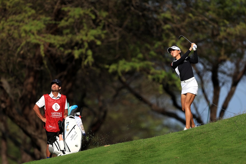 Lydia Ko joue un coup sous le regard de son caddie, avec des arbres en arrière-plan