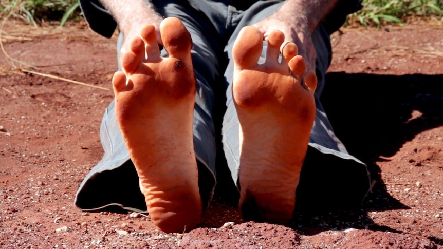 The bottom of bare feet with red dirt on them