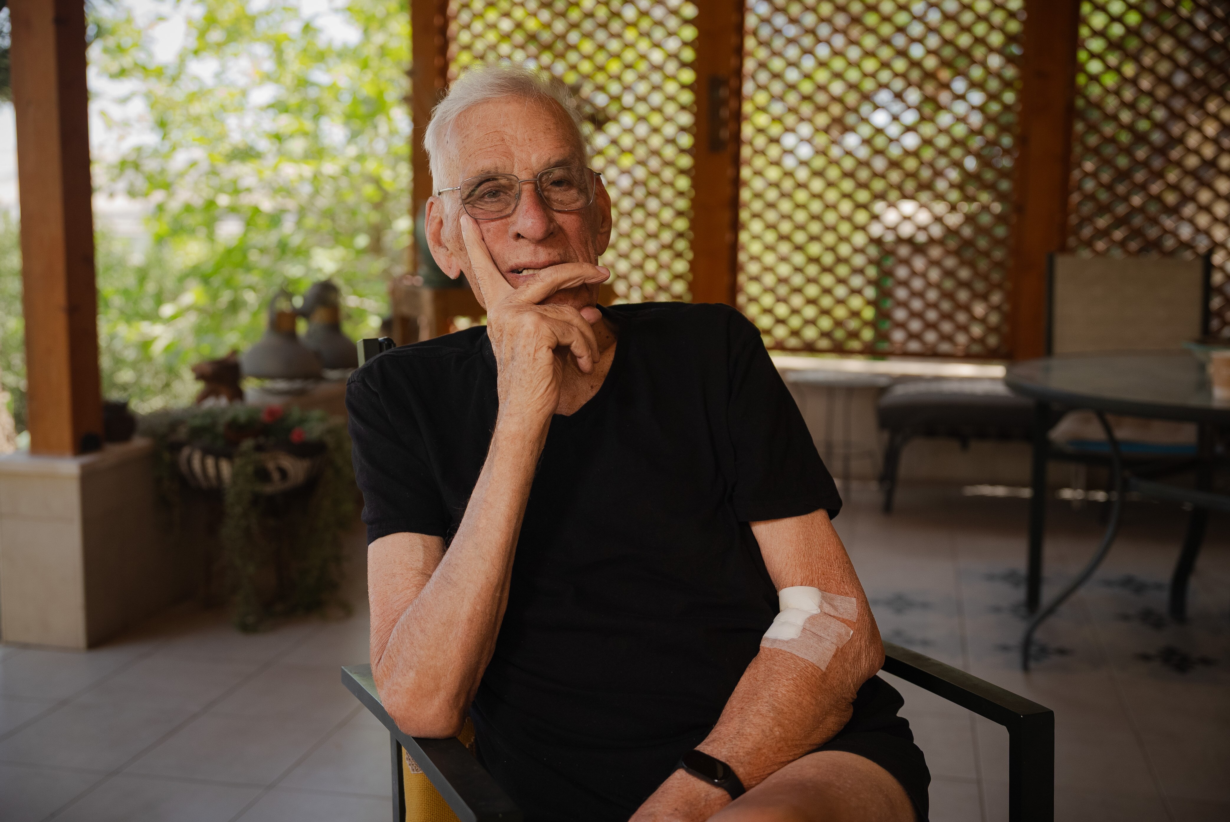 An older man in a black T-shirt looks thoughtful.