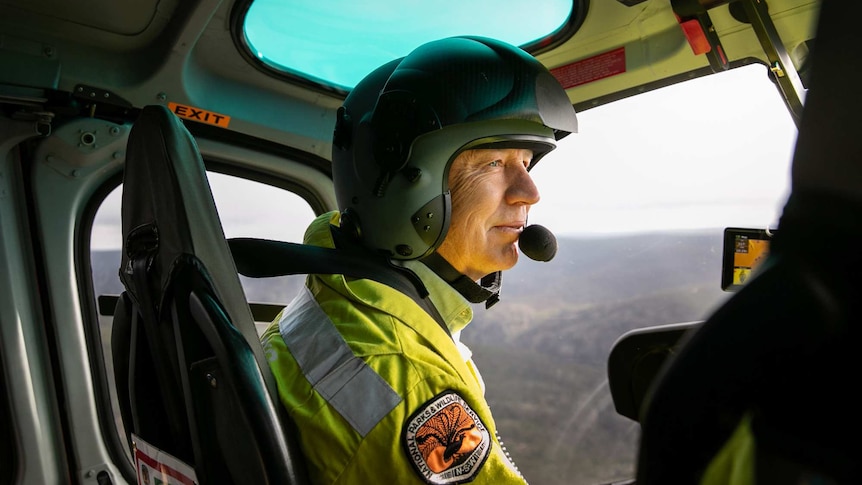 A man with a helmet on looking out the front of a helicopter