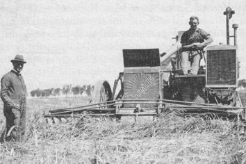Headlie Taylor stands in a field next to the Sunshine Auto Header that he designed in 1924. A worker sits atop the auto header.